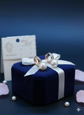 Rose gold hoop earrings with hanging white pearls displayed on navy velvet gift box with white ribbon.