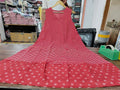 Sleeveless red dress with white stripes and floral border, hanging on wooden hanger.