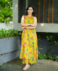 Yellow sleeveless dress with colorful floral print and asymmetrical hem worn with sandals.