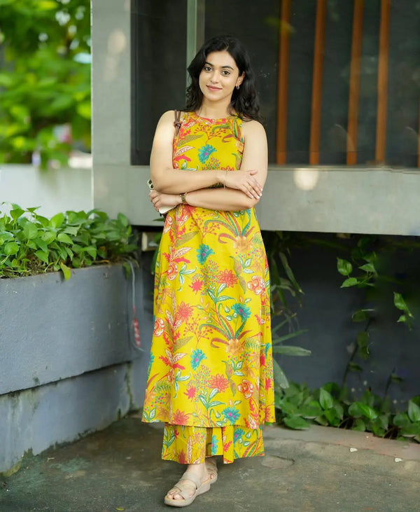 Yellow sleeveless dress with colorful floral print and asymmetrical hem worn with sandals.