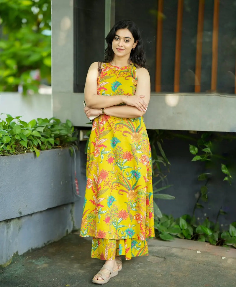 Yellow sleeveless dress with colorful floral print and asymmetrical hem worn with sandals.