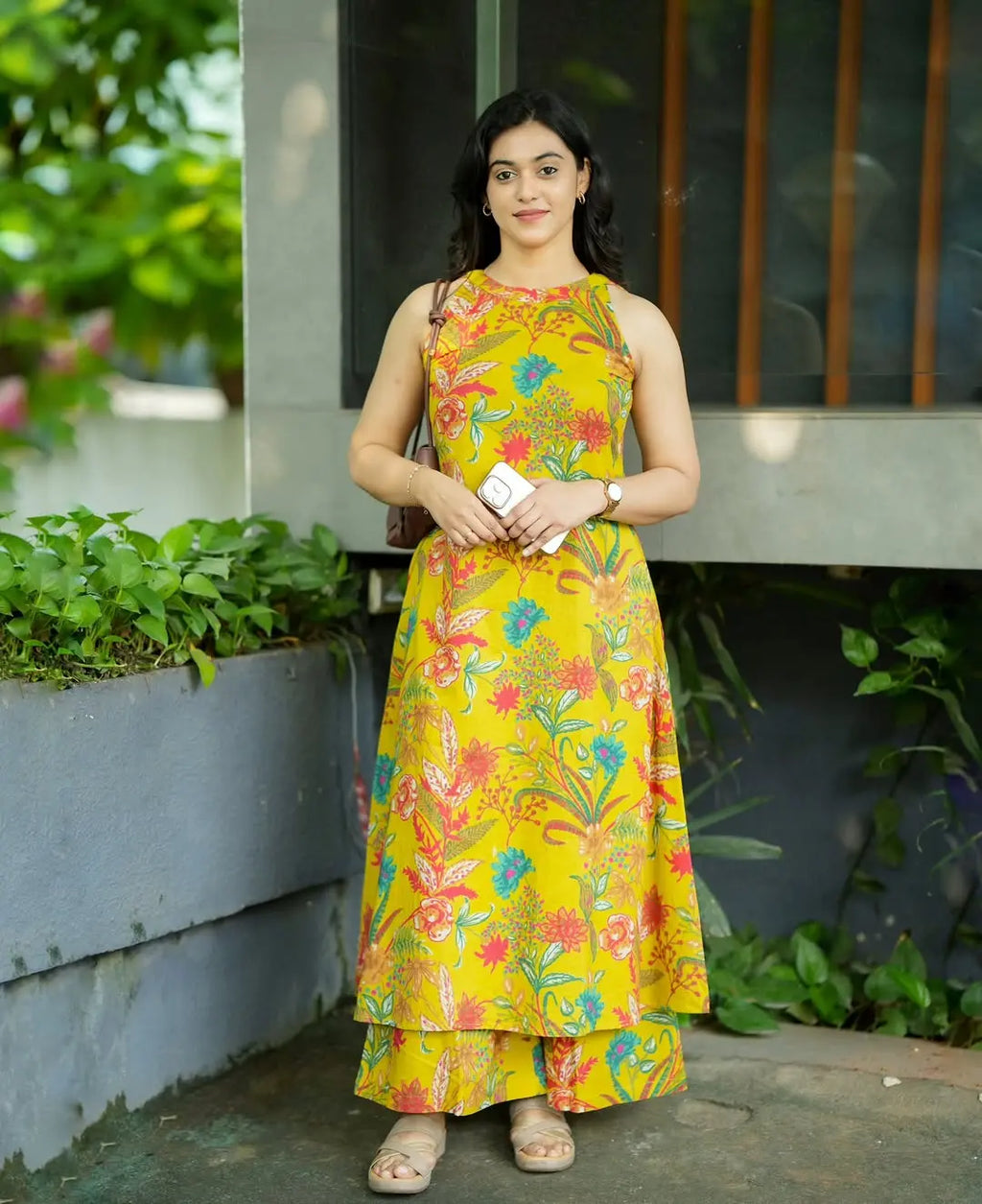 Yellow sleeveless dress with colorful floral print and tiered hem, modeled outdoors.