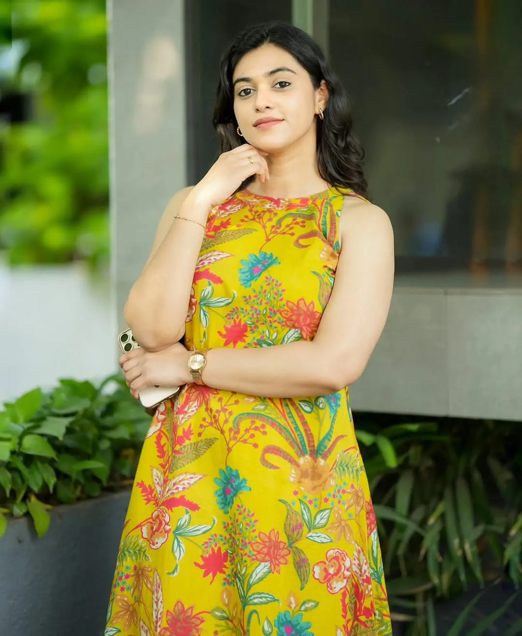 Sleeveless yellow dress with colorful floral and paisley print, fitted waist, worn by woman.