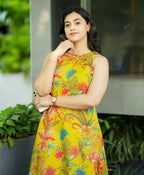 Sleeveless yellow dress with colorful floral and paisley print, fitted waist, worn by woman.