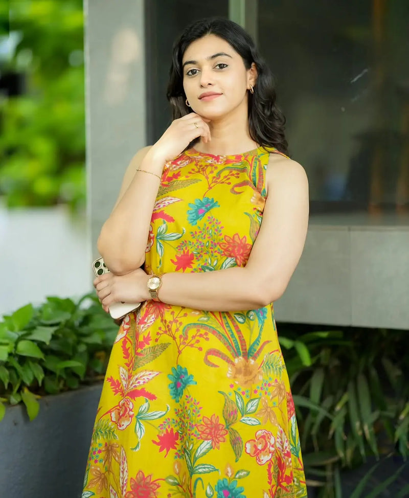 Sleeveless yellow dress with colorful floral and paisley print, fitted waist, worn by woman.