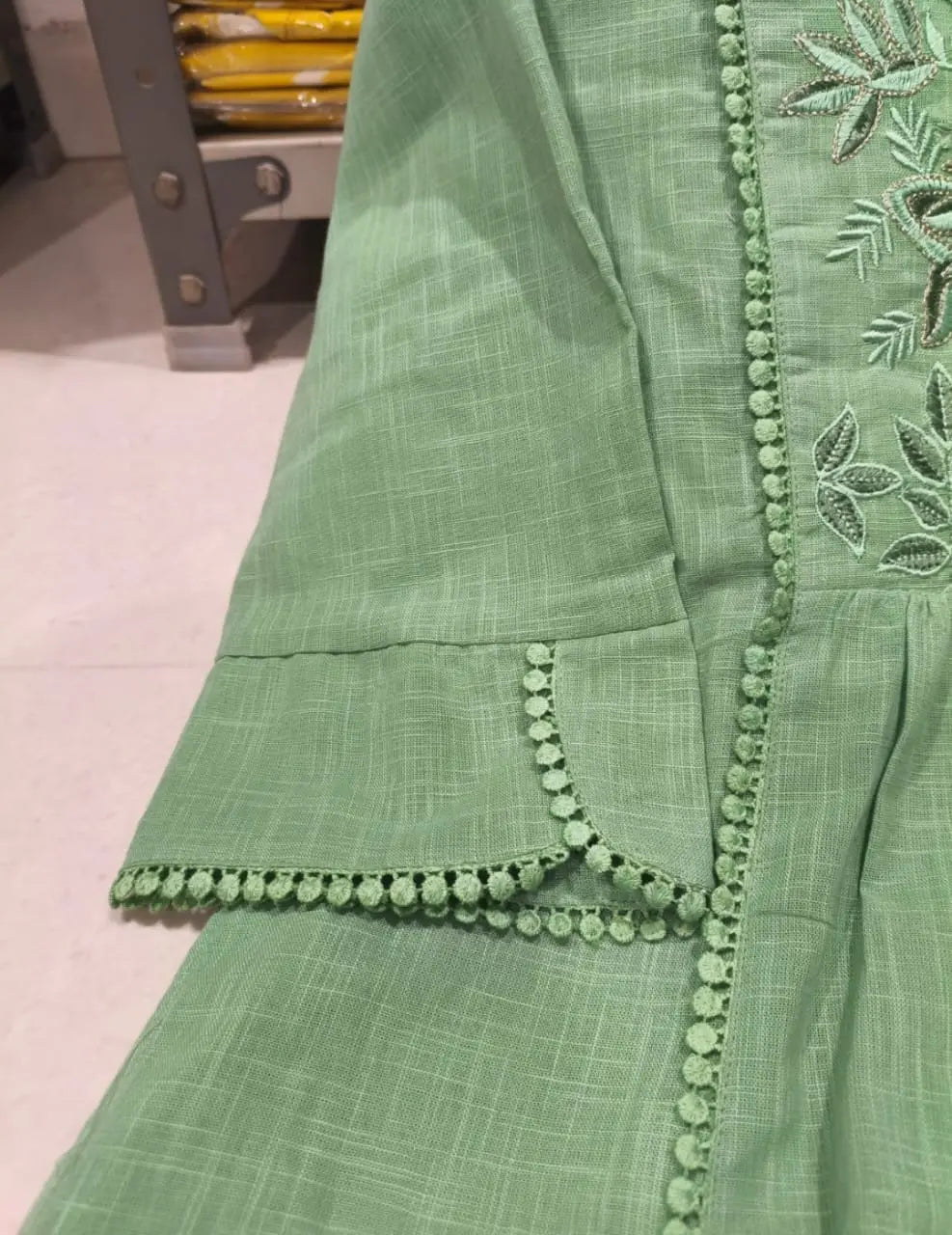 Light green kurta sleeve with floral embroidery and pom-pom trim on cuff.