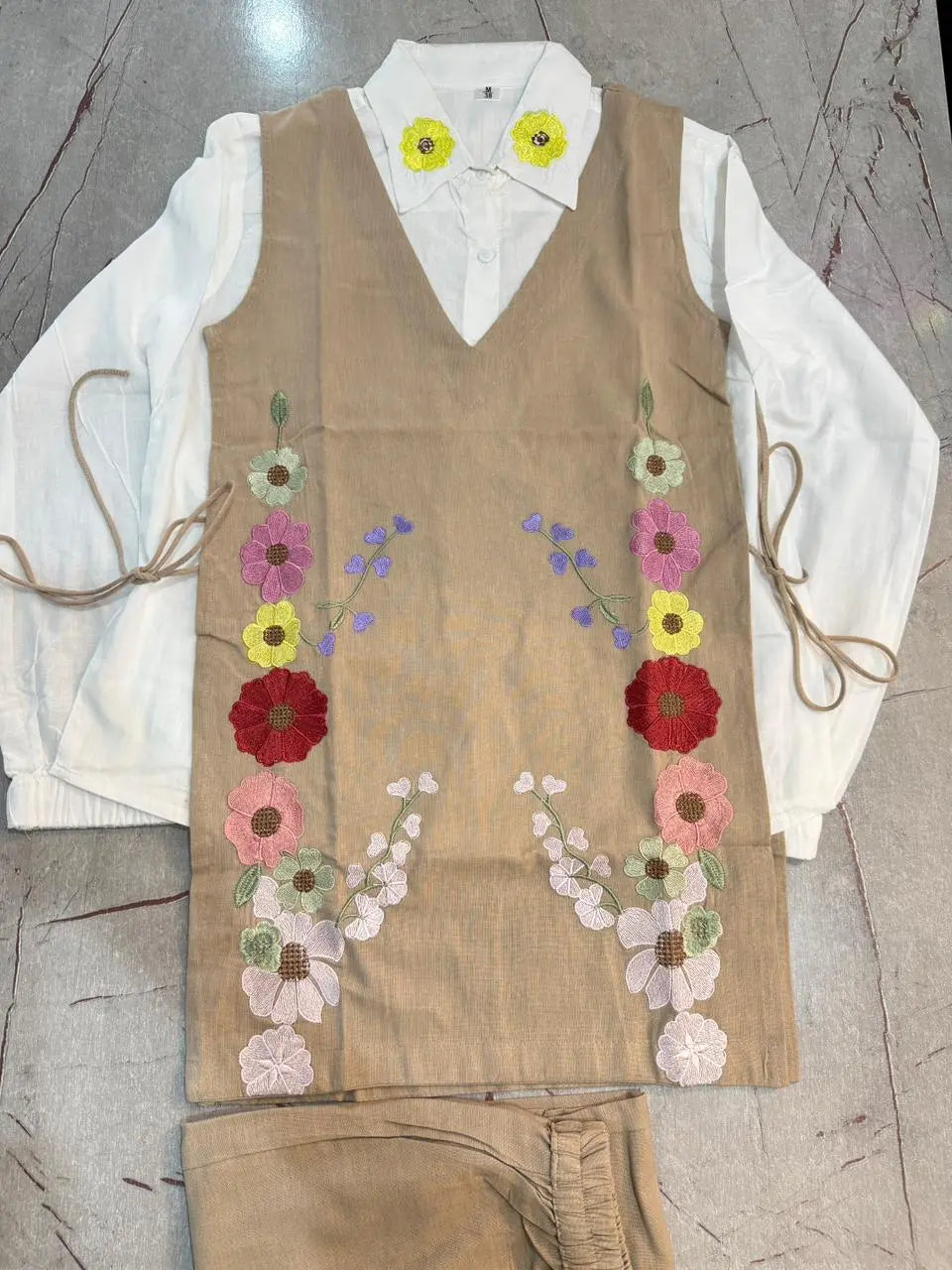 Beige linen corset with colorful floral embroidery over white long-sleeve blouse.