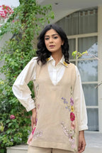Beige floral embroidered corset layered over white long-sleeve collared blouse.