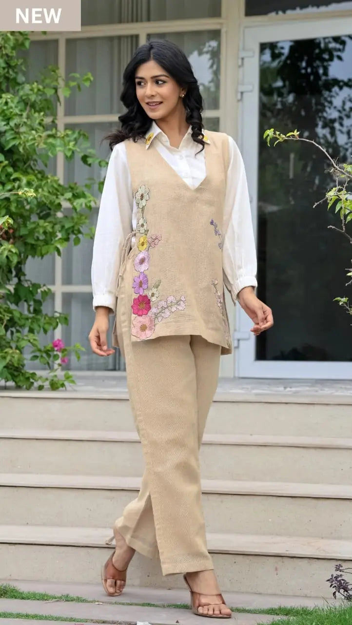 Beige sleeveless corset with floral embroidery over white long-sleeve blouse and matching beige pants.