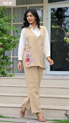 Beige sleeveless corset with floral embroidery over white long-sleeve blouse and matching beige pants.