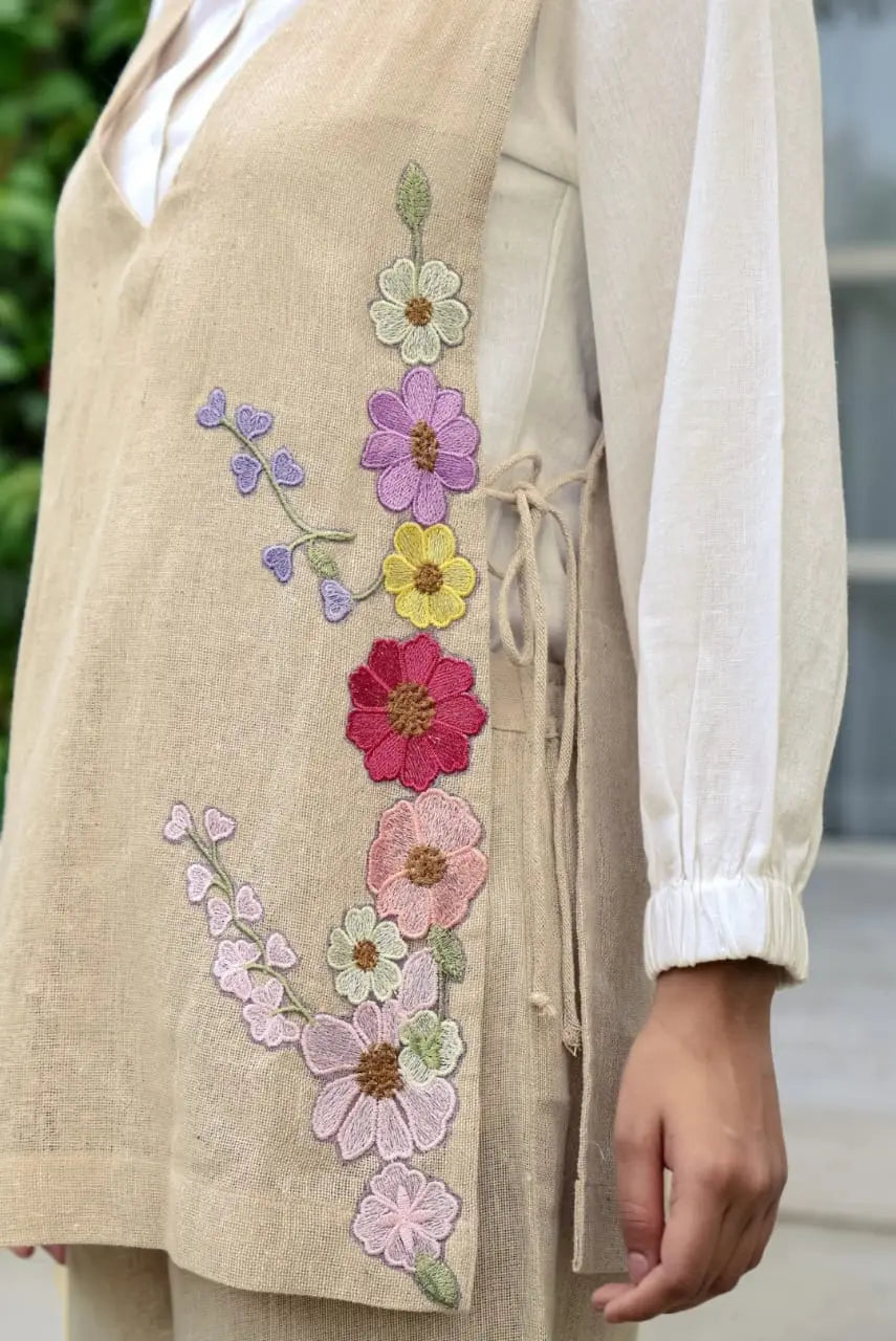 Beige corset with colorful embroidered flowers and side lace-up detail over white blouse.