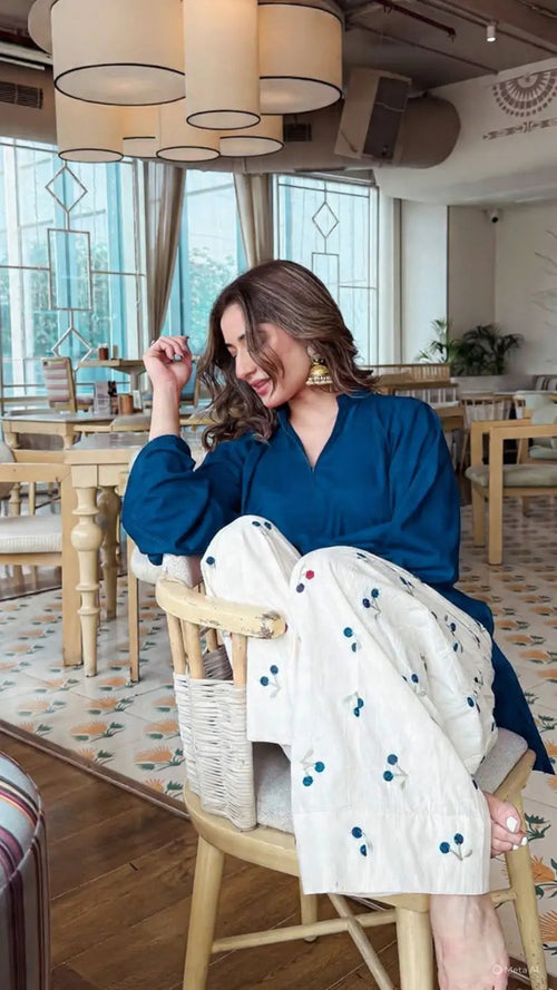 Blue long-sleeve corset-style top with v-neck worn by model sitting in wooden chair.
