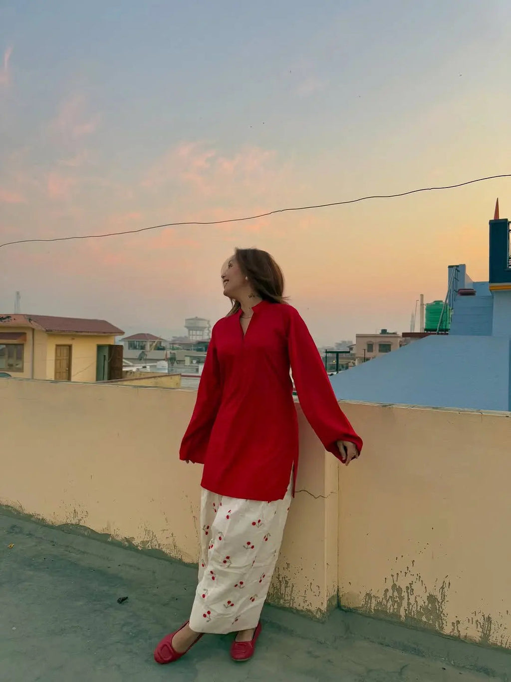 Woman wearing long-sleeve red corset top with flowy sleeves and floral skirt during sunset outdoors.