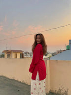 Red fitted corset with long sleeves worn over a white skirt with red floral print at sunset.