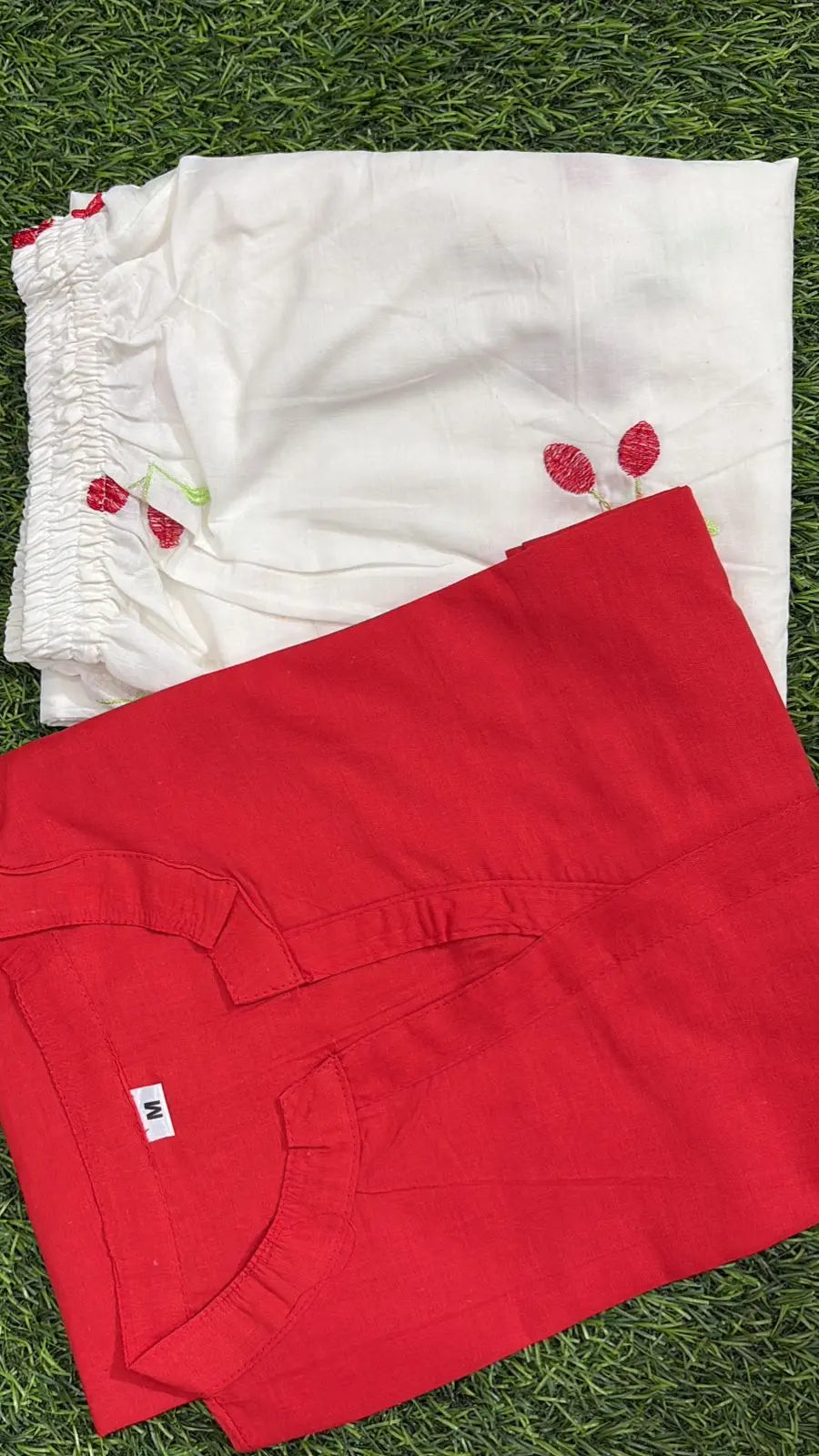 Red corset-style top with front lace-up detail, laid flat on green grass.