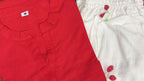 Red sleeveless corset with V-neck and button detail next to white fabric with red floral embroidery.