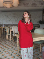 Red corset with structured boning worn over long-sleeve red blouse and white pants with red floral print.