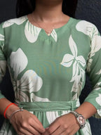 Green dress with large white floral print, round neckline, long sleeves, and a waist tie belt.