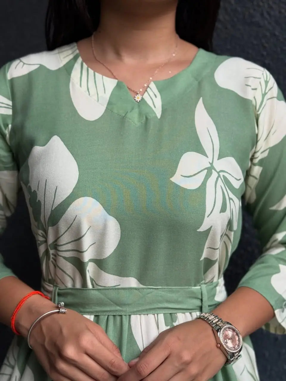Green dress with large white floral print, round neckline, long sleeves, and a waist tie belt.