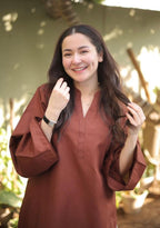 Brown long-sleeve tunic with wide sleeves and a v-neck worn by smiling woman outdoors.