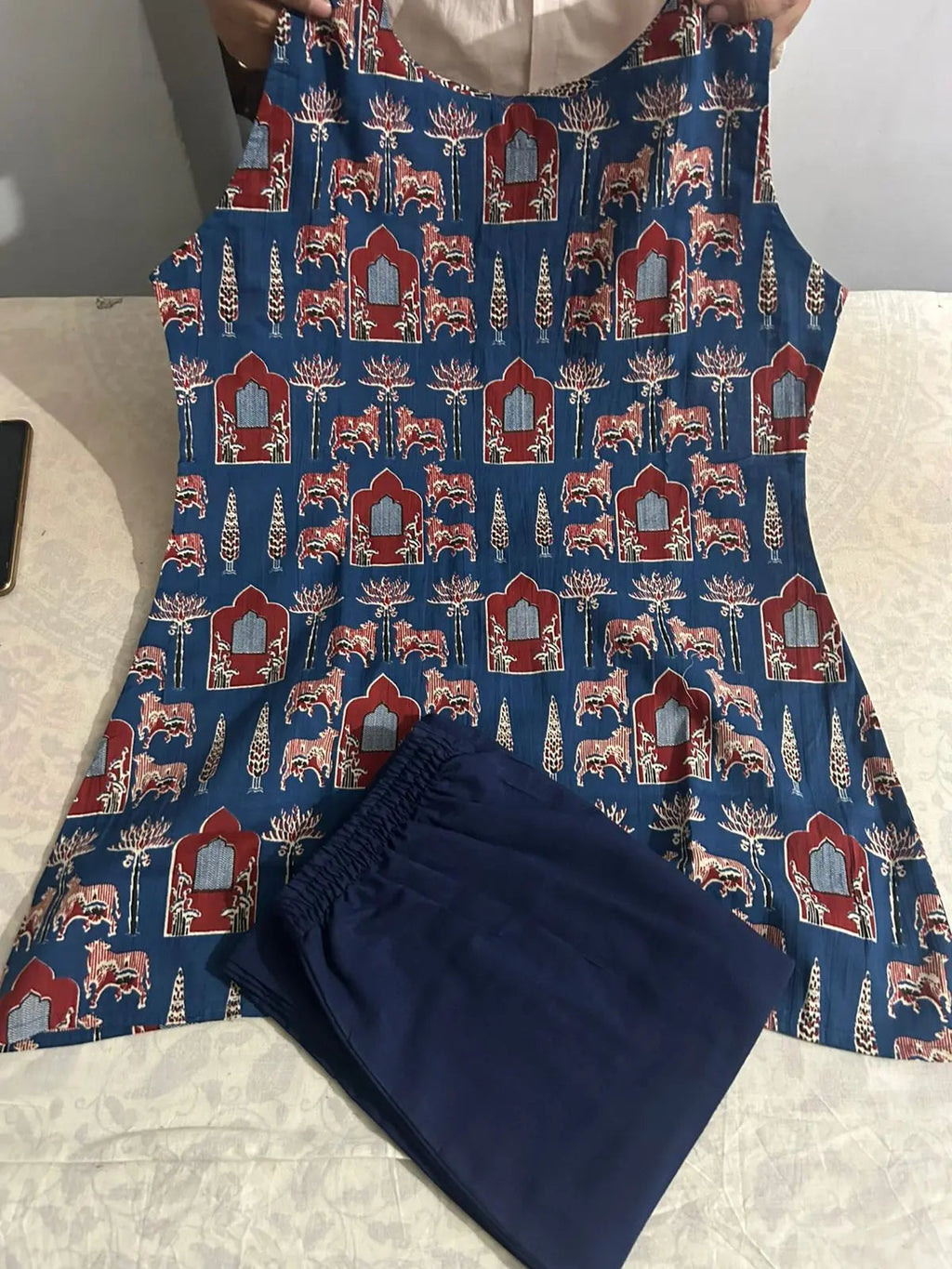 Blue and red patterned sleeveless dress with floral and geometric motifs paired with navy blue pants.