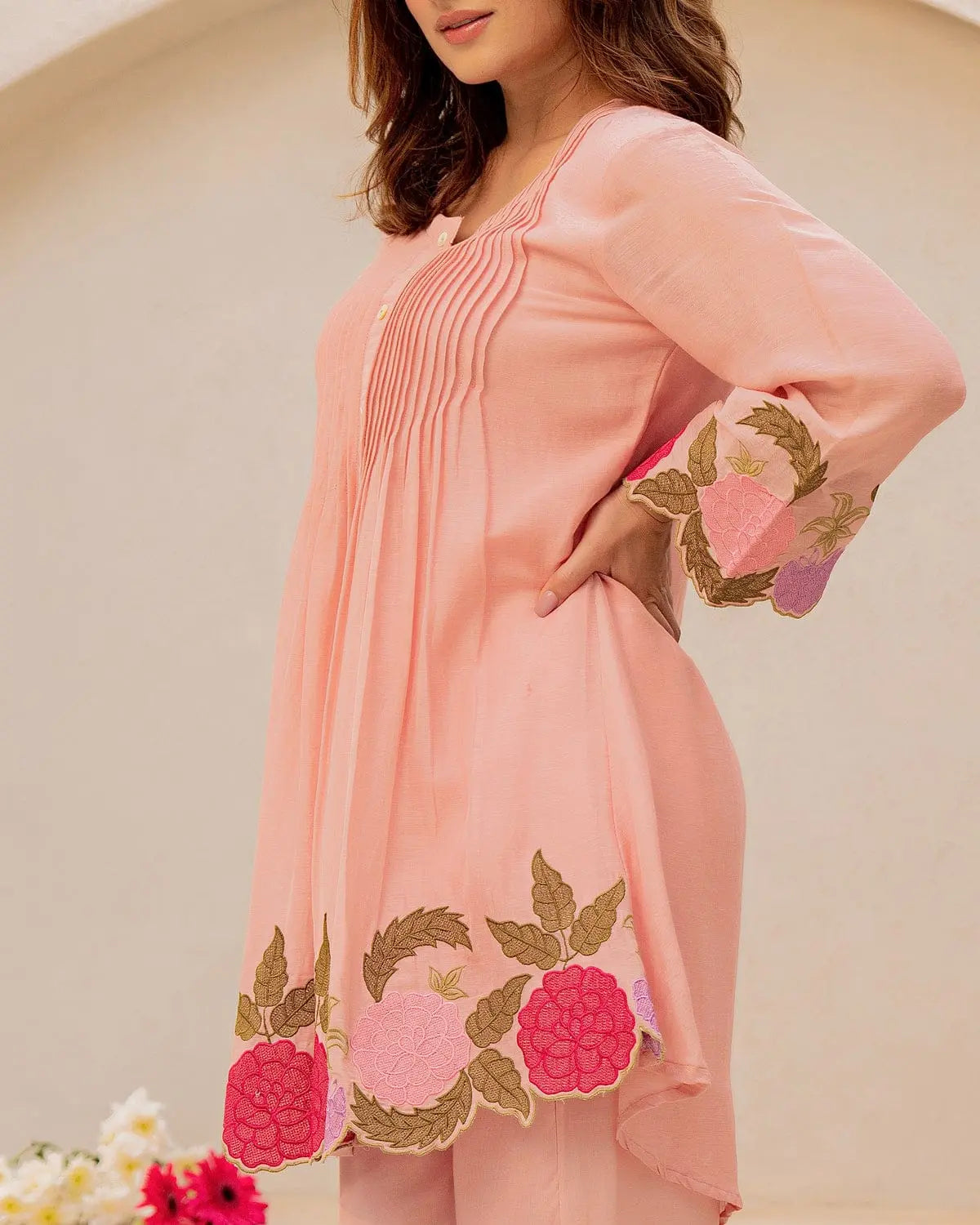 Peach cotton kurta with pink and green floral embroidery on sleeves and hem, featuring front pleats.