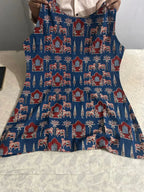 Blue apron with red, white, and beige intricate floral and geometric patterns, tied at the waist.