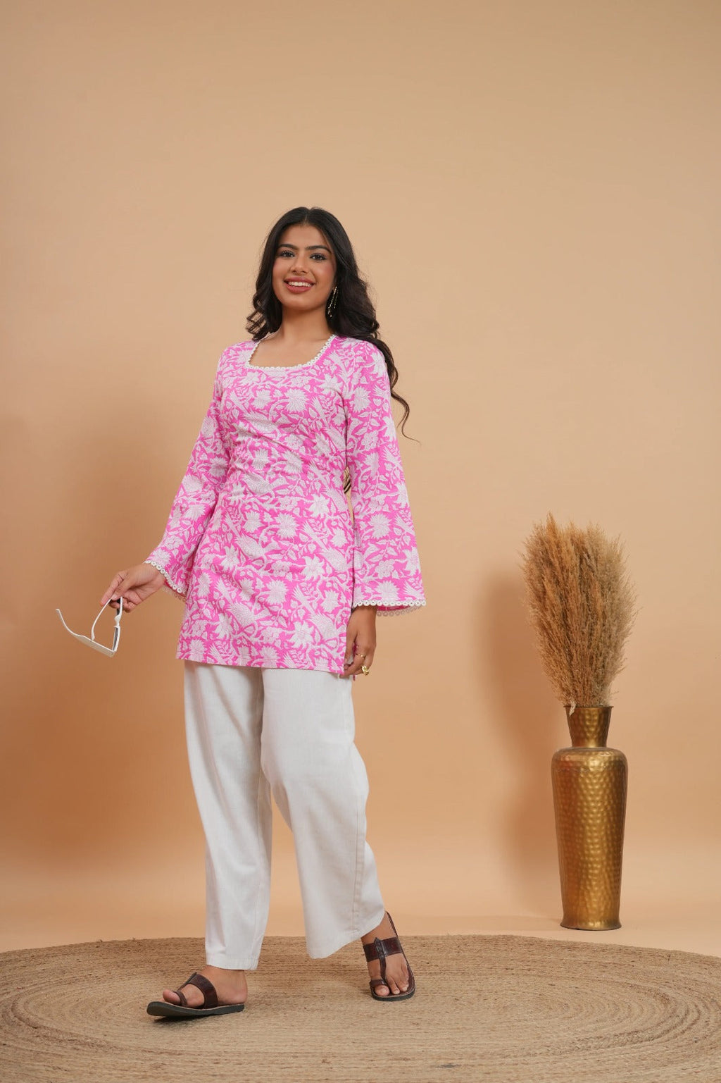 Pink floral short kurti top with bell sleeves paired with white pants and black sandals.