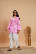 Pink floral short kurti top with bell sleeves paired with white pants and black sandals.