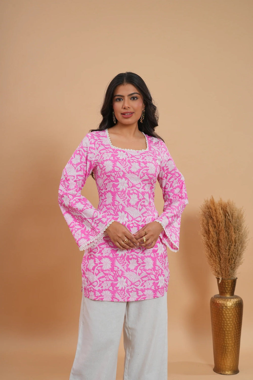 Pink floral short kurti with long sleeves and square neckline, paired with white pants.