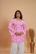 Pink floral short kurti with long sleeves and square neckline, paired with white pants.