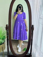 Purple midi dress with short sleeves, button front, and white floral embroidery paired with white sneakers.
