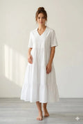 White midi dress with V-neck, short sleeves, and tiered skirt on a standing model.
